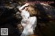 A woman in a white dress sitting on a rock in the water.