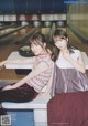 Two young women sitting on a bench in a bowling alley.