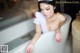 A woman in a white nurse outfit sitting in a bathtub.