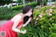 A woman in a red dress smelling a flower.