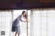 A woman standing in front of a window with sheer curtains.