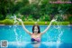 A woman in a bikini splashing water in a swimming pool.