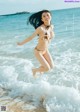 A woman in a bikini jumping into the ocean.