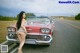 A woman standing next to a red car on the side of the road.